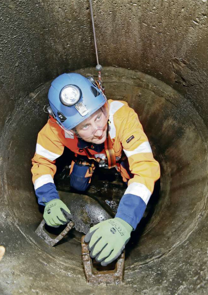 Kanalarbeiter der in einen Abwasserschacht steigt